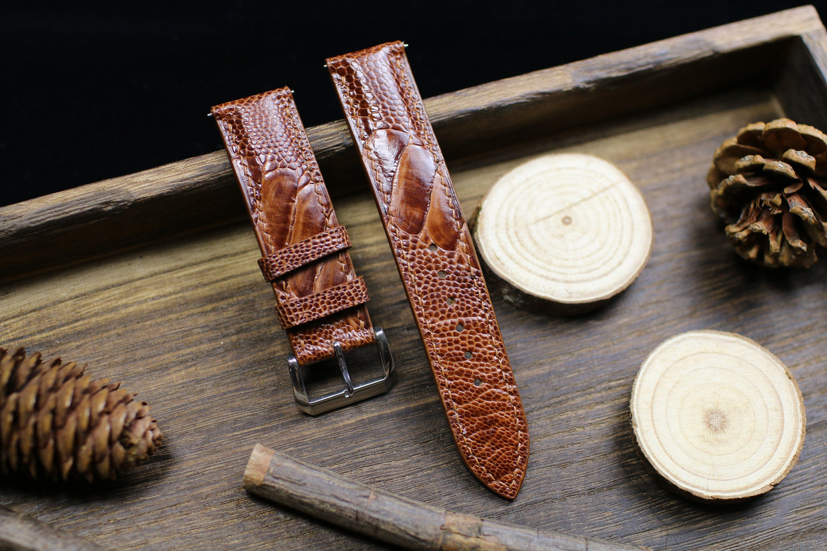 British tan ostrich leg leather watch strap with large scales on a wooden tray